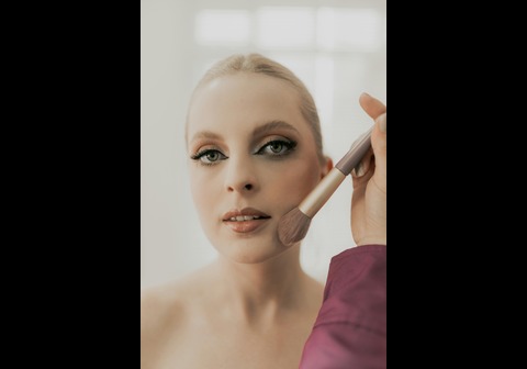 A makeup artist applying powder to a woman's cheek with a makeup brush.